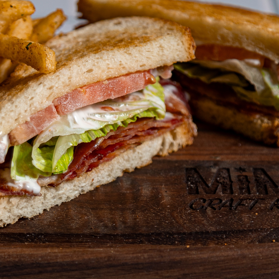A MiMi's Craft Kitchen BLT sandwich with fries on a wooden board.