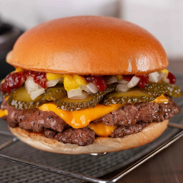 A MiMi's Craft Kitchen double cheeseburger with pickles, onions, ketchup, and mustard on a bun.