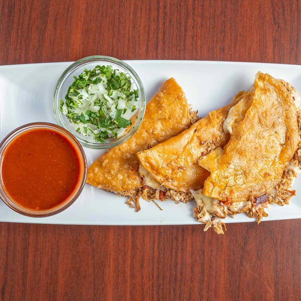 Three golden-brown quesadillas filled with shredded meat and melted cheese, served with salsa and chopped onions.