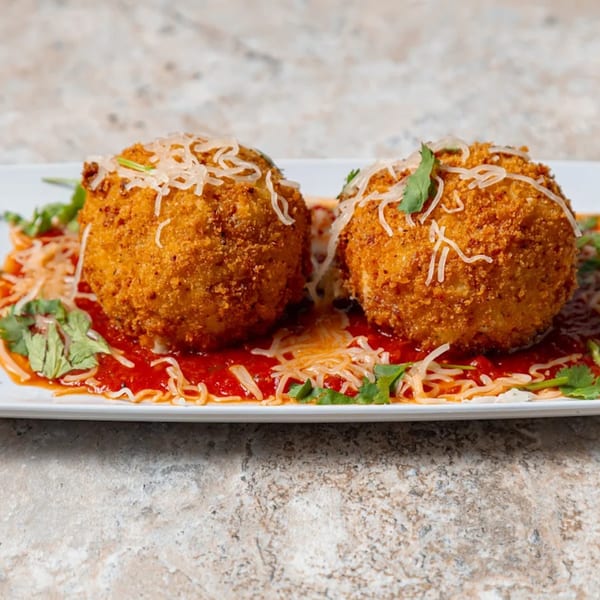 Two golden-brown arancini balls topped with shredded cheese and parsley, served on red sauce.