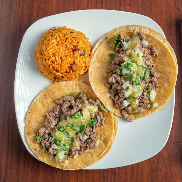Two MiMi's Craft Kitchen beef tacos with salsa verde, onions, cilantro, and a side of rice.